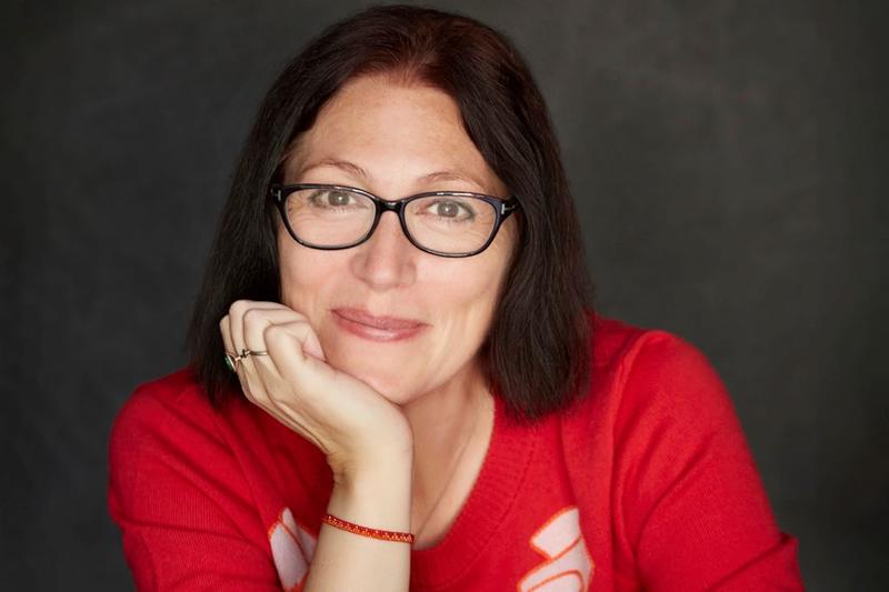 head and shoulders photo of natalie haynes looking directly at the camera smiling with her chin in her left hand